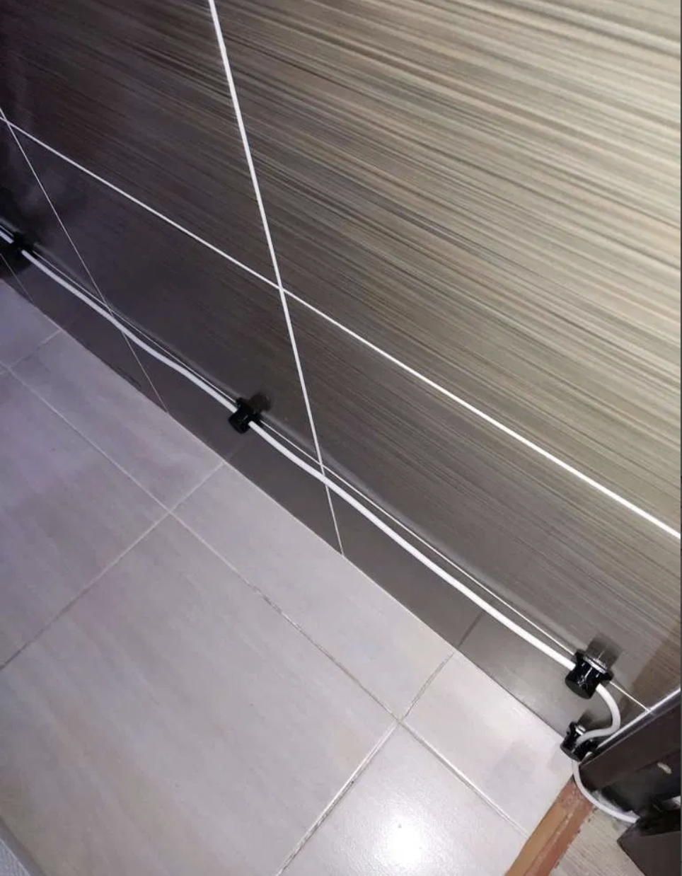 Printed clips running a white cable neatly along the edge of a tiled floor