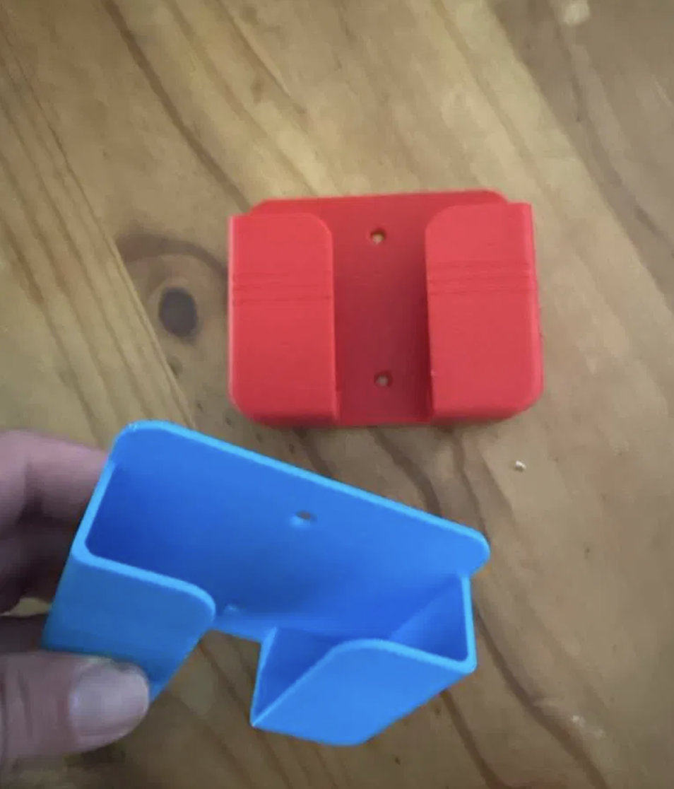 Two printed wall mounts for phones, one red and one blue, held in a hand