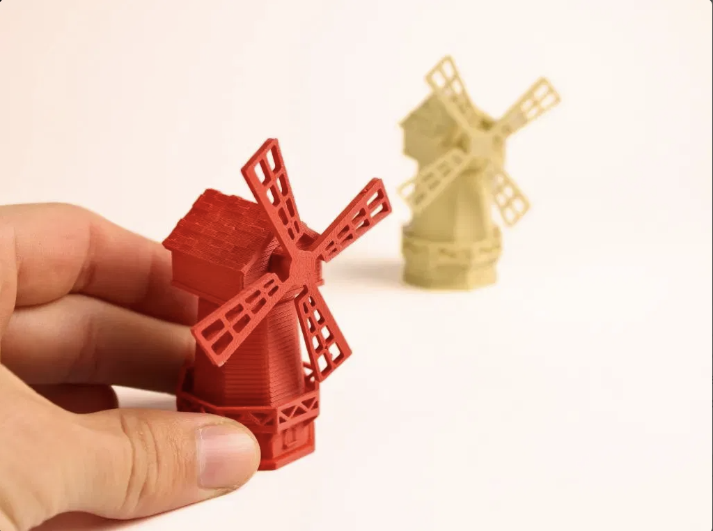 Two miniature printed windmills, a red one held between finger and thumb